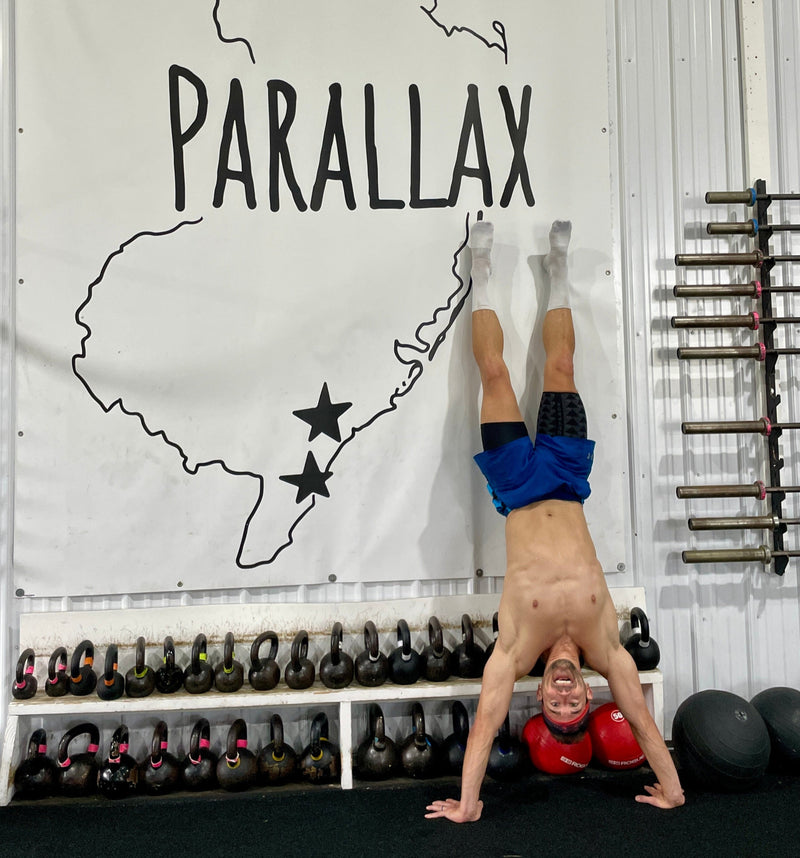 Me doing a handstand in a gym with 'Parallax' branding on a large map of Maine.